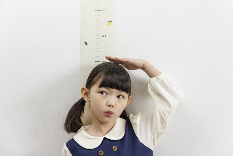 벽에 등을 대고 손으로 키를 재는 아이