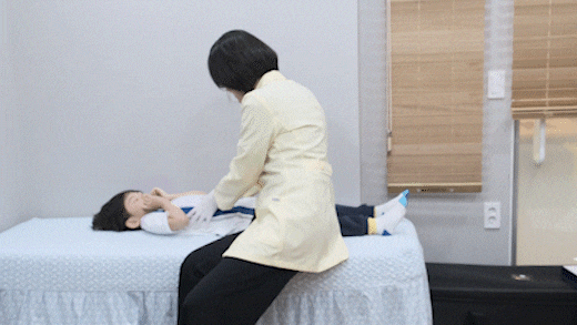 진료실 침대에 누운 아이를 한의사가 살펴보는 모습