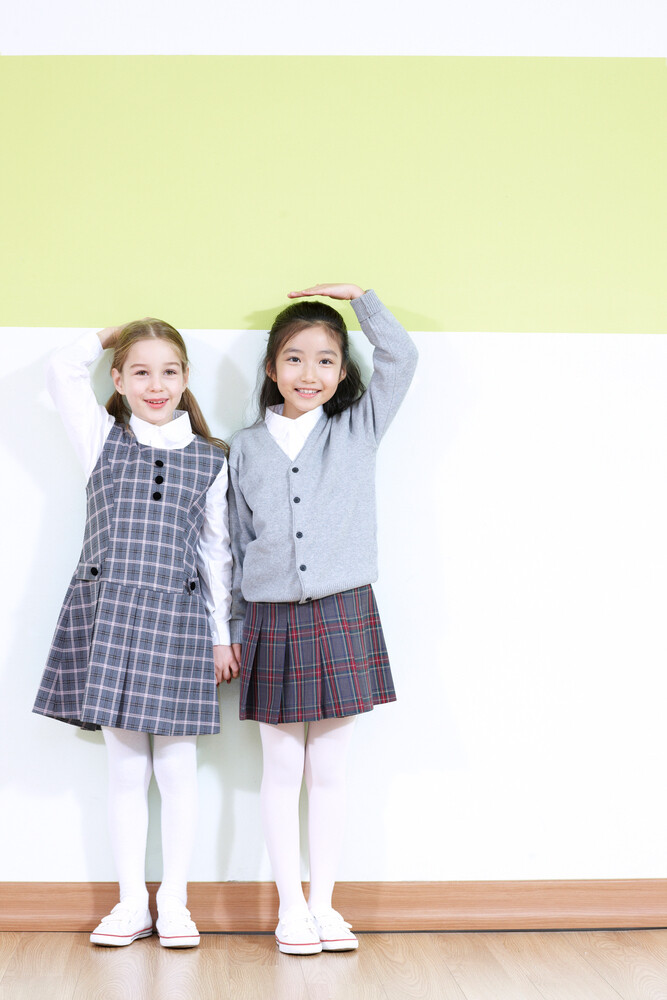 벽에 등을 대고 나란히 서서 키를 재는 두 아이